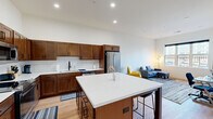 Located at 3830 Joliet Trail in Sheboygan, WI, this thoughtfully designed one-bedroom, two-bathroom residence offers a well-appointed single-floor layout with modern finishes and a functional open-concept design. The kitchen is a standout feature, showcasing rich, warm-toned cabinetry, crisp white quartz countertops with a classic subway tile backsplash, stainless steel appliances, and a generously sized center island with bar seating — ideal for casual dining or entertaining. Light hardwood flooring flows throughout the main living areas, complementing the neutral palette and recessed lighting overhead. The living room offers a comfortable, airy feel with a large window that brings in natural light and views of the surrounding neighborhood. The bedroom is carpeted and well-sized, featuring a walk-in closet and a window that further enhances the bright ambiance. Two bathrooms serve the space, including one with a vanity finished in matching warm wood tones, a large mirror, and clean, modern fixtures, and a second with a shower-tub combination. A stacked in-unit washer and dryer adds everyday convenience. The overall design balances modern aesthetics with practical living in a compact yet efficient footprint.