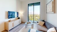 Located in Miami's vibrant Wynwood district, this thoughtfully designed one-bedroom, one-bathroom residence offers a sleek, modern aesthetic across a well-utilized single-floor layout. Light wood flooring flows throughout, complemented by bright white walls and abundant natural light streaming through floor-to-ceiling windows.

The open-concept kitchen and living area form the heart of the home. The kitchen features light wood cabinetry extending to the ceiling, white quartz countertops, stainless steel appliances including a side-by-side refrigerator, electric range, and built-in microwave, and a central island with bar seating illuminated by globe pendant lights with brass accents. The living room opens directly to a private balcony through expansive sliding glass doors, offering sweeping views of Miami's lush canopy and cityscape.

The bedroom is a serene retreat, bathed in natural light from its own floor-to-ceiling window wall framing the same scenic outdoor views. A dedicated closet provides practical storage. The bathroom is finished with a wood-toned vanity, white quartz countertop, an LED-backlit mirror, and neutral tile flooring. Additional conveniences include an in-unit laundry area and a utility room, rounding out this well-appointed urban residence.