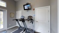 Located at 6300 Caleb's Creek Way in Westerville, Ohio, this fitness center offers a clean and functional workout environment designed to support an active lifestyle. The space is finished with neutral gray walls and carpeted flooring, creating a practical yet comfortable atmosphere for exercise. The cardio area is equipped with multiple treadmills, each featuring individual digital display consoles for tracking workout metrics. A wall-mounted flat-screen television is positioned above the equipment, allowing residents or members to stay entertained during their workout sessions. The room is well-organized, with clearly marked accessible restroom facilities conveniently located directly within the fitness space, ensuring ease of access for all users. Accessibility signage is prominently displayed throughout, reflecting a commitment to inclusive design. The single-floor layout provides a straightforward, no-frills environment focused on delivering essential fitness amenities. The overall ambiance is tidy and purposeful, making it a practical resource for daily exercise routines.