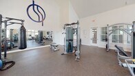 Located at 8115 Dougherty Ct in Travelers Rest, SC, this single-floor fitness center is designed to provide a complete workout experience in a bright, open environment. The space is defined by its striking vaulted ceilings, which soar to impressive heights and lend the room a spacious, airy feel. Rows of windows along the walls, including clerestory windows near the roofline, flood the interior with natural light and create an inviting atmosphere throughout.

The rubber-floored workout area is thoughtfully organized to accommodate a wide variety of exercise modalities. The cardio section features multiple treadmills, a stationary spin bike, and a rowing machine, all positioned to take advantage of the natural light. Strength training is well-represented with a cable functional trainer, a multi-use cable machine, a weight bench, and a well-stocked dumbbell rack. A wall-mounted flat-screen television provides entertainment during workouts.

A large wall mirror enhances the sense of space while allowing users to monitor their form. The clean, white walls and neutral tones throughout contribute to a fresh, motivating ambiance. The facility is neatly maintained and thoughtfully laid out, ensuring ample open floor space for movement and stretching. This fitness center offers residents a professional-grade workout environment close to home.