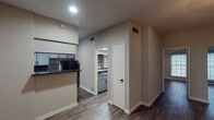 This single-story unit in Houston, TX offers a practical and cohesive design highlighted by dark hardwood-style flooring that runs consistently throughout the space. The open layout connects the living area to the kitchen, creating a functional flow ideal for everyday living.

The living area greets residents with a paneled entry door and a large window fitted with horizontal blinds, allowing natural light to fill the room. A ceiling light fixture anchors the space overhead.

The kitchen features gray cabinetry with bronze hardware, dark granite-style countertops, a tiled backsplash, a stainless steel double sink, and a black electric range. Upper and lower cabinets provide ample storage, while a window above the sink brings in additional natural light.

The bedroom is a standout space, featuring two arched windows that flood the room with natural light, a ceiling fan, and access to a walk-in closet. The vaulted ceiling adds a sense of openness and volume.

The bathroom includes a tub-shower combination with white tile surround accented by a dark tile border, complemented by wood-style flooring. The unit's neutral gray walls throughout create a clean, cohesive aesthetic well-suited for a variety of furnishing styles.