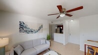 This single-floor residence offers a well-organized layout that connects the living, dining, and kitchen areas in an open, cohesive flow. The living room is characterized by light tile flooring, crisp white walls, and a ceiling fan with a built-in light fixture. A window with horizontal blinds allows natural light to filter in while providing a view of the surrounding greenery. A textured accent wall serves as a focal point behind the seating area, adding visual depth to the space.

The kitchen is efficiently designed with rich, dark wood cabinetry, granite countertops, and stainless steel appliances including a refrigerator, electric range, and over-the-range microwave. A peninsula with an undermount sink and pendant lighting above doubles as a casual dining or prep surface, creating a functional connection between the kitchen and living areas.

The two bedrooms each feature ceiling fans, light tile flooring, and windows that bring in natural light. Both rooms offer closet storage and a calm, neutral palette. The bathroom includes a dark-framed vanity mirror, white countertop, and a tiled shower, maintaining a clean and functional aesthetic consistent with the rest of the home.