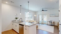 Located at 660 Aubrey Ln in Calabash, NC, this single-story, 3-bedroom, 2-bathroom home offers a well-designed layout with a bright, modern aesthetic. The open-concept kitchen and living area serves as the heart of the home, featuring a granite-topped island with bar seating, white cabinetry with matte black hardware, stainless steel appliances, and sleek pendant lighting. Light wood-look flooring flows throughout, complementing the crisp white walls and abundant natural light from multiple windows. The living area is comfortably sized and connects seamlessly to the kitchen, with a ceiling fan overhead and French doors providing additional natural light. The primary bedroom includes a walk-in closet with wire shelving and easy access to the hallway. All bedrooms are finished in the same clean, neutral palette with ceiling fans and ample closet storage. Two full bathrooms serve the home, one featuring a tub-shower combination with clean white surroundings and wood-look flooring. A dedicated laundry area, utility room, and three closets add practical storage throughout. The hallway connects all rooms efficiently, maintaining an open and airy feel. This home combines functional design with modern finishes in a compact, easy-to-navigate floor plan.