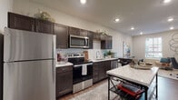 Located at 114 E Fifth Ave in Columbus, Ohio, this single-floor residential unit offers a thoughtfully designed layout that balances functionality and contemporary style. The kitchen is a standout feature, showcasing rich dark-espresso cabinetry with shaker-style doors, light stone countertops, a classic white subway tile backsplash, and a full suite of stainless steel appliances including a refrigerator, range, over-the-range microwave, and dishwasher. Wood-look plank flooring runs throughout the kitchen and main living areas, adding warmth and cohesion to the space. The living area is bright and welcoming, benefiting from a large window dressed with white blinds that allow natural light to fill the room. Neutral wall tones create a versatile backdrop throughout. The bedroom is a comfortable retreat, featuring plush carpet, a generously sized window with views of the surrounding neighborhood, and soft, neutral finishes. The bathroom is finished with elegant marble-look tile in the walk-in glass-enclosed shower, dark wood vanity cabinetry, and durable wood-look flooring, lending a clean and modern aesthetic. Recessed lighting throughout the unit provides consistent, well-distributed illumination, contributing to the overall polished and contemporary feel of the home.