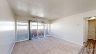 Located in Arden-Arcade, California, this efficient one-bedroom, one-bathroom unit offers a thoughtfully organized single-floor layout that maximizes every inch of its compact footprint. The open-plan living, dining, and kitchen area forms the heart of the home, creating a seamless flow between spaces. The living and dining area is finished with plush carpet and features a sliding glass door flanked by windows, filling the room with natural light and providing direct access to an outdoor space. The kitchen is appointed with white cabinetry, dark granite-style countertops, wood-look flooring, a stainless steel gas range, and a double-basin sink — all complemented by multiple windows that keep the space bright and airy. A hallway connects the main living area to the private bedroom, which is a well-proportioned retreat carpeted for comfort and fitted with a double sliding-door closet plus an additional closet for generous storage. The full bathroom features wood-look flooring, a white vanity with dark countertop, a large mirror, and a tub/shower combo with clean white tile surround. Textured ceilings and neutral wall tones throughout give the space a clean, cohesive aesthetic.
