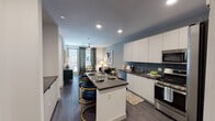 This single-floor residence showcases a thoughtfully designed open-concept layout that seamlessly connects the kitchen, dining, and living areas. The kitchen is a standout feature, outfitted with floor-to-ceiling white cabinetry, dark subway tile backsplash, dark quartz countertops, and a full suite of stainless steel appliances including a gas range, over-the-range microwave, dishwasher, and refrigerator. A central island with seating provides an ideal casual dining or entertaining space, complemented by wood-style flooring that runs throughout the main living areas.

The living area extends toward large windows dressed with patterned drapes, allowing generous natural light to fill the space. A ceiling fan adds both function and comfort to this zone.

The bedroom offers a serene retreat, featuring plush carpeting, a bold teal accent wall, and a large window that invites natural light. A ceiling fan enhances airflow, while ample space accommodates a full furniture arrangement comfortably.

The bathroom is finished with dark wood-tone cabinetry, a single undermount sink with modern fixtures, and dark countertops. A walk-in closet is directly accessible from the bathroom, offering organized storage with built-in shelving and hanging space. Recessed lighting throughout the unit contributes to a clean, contemporary ambiance.