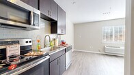 Located at 1374 Fording Island Rd in Bluffton, South Carolina, this single-floor unit offers a thoughtfully designed layout with modern finishes throughout. The kitchen serves as a functional centerpiece, showcasing rich dark cabinetry, a classic subway tile backsplash, stainless steel appliances including a range, built-in microwave, and dishwasher, as well as a stainless steel sink with a contemporary pull-down faucet. A small breakfast bar extends the counter space, providing a casual dining option. Light hardwood-style flooring runs throughout the unit, creating a cohesive and clean aesthetic that complements the neutral, warm-toned walls. The living area is bright and open, benefiting from natural light that filters in through the windows, casting soft patterns across the floor. The space offers a versatile, flexible layout. The bathroom is well-finished, featuring a bold navy vanity with a vessel sink, a framed mirror, subway tile accents, and a combined tub and shower with marble-style tile surround. Additional details include white panel doors, clean white baseboards, and a wall-mounted HVAC unit. The overall ambiance is modern, clean, and move-in ready, reflecting contemporary residential design suited for comfortable everyday living.