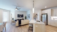 This single-floor residence is designed with a contemporary aesthetic, combining functionality and style across its well-appointed layout. The open-concept main living area serves as the centerpiece of the unit, where the kitchen, dining, and living spaces flow seamlessly into one another. The kitchen is equipped with stainless steel appliances, including a refrigerator, range, and microwave, complemented by light wood cabinetry extending to the ceiling and granite countertops. A peninsula with bar seating and pendant lighting above adds both practicality and visual appeal. The living area features light hardwood-style flooring, a ceiling fan, and ample space for comfortable furnishings, while a designated dining nook accommodates a small table and chairs.

The unit includes two bedrooms, each carpeted and fitted with ceiling fans. Both bedrooms offer access to walk-in closets, providing generous storage. The bathrooms maintain the unit's cohesive design language, featuring granite-topped vanities with light wood cabinetry, hardwood-style flooring, and clean white fixtures. One bathroom includes a tub-shower combination, while another features a standalone vanity setup. Neutral wall tones and recessed lighting throughout contribute to a bright, welcoming ambiance.