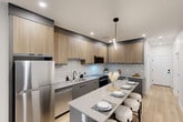 Located in the heart of Calgary's downtown at 8th Avenue SW, this contemporary 2-bedroom, 2-bathroom residence offers a well-appointed layout with modern finishes throughout. Light wood-toned flooring runs through the unit, complemented by crisp white walls and recessed lighting that create a clean, bright atmosphere.

The kitchen is a standout feature, showcasing two-tone cabinetry with natural wood uppers and charcoal grey lowers, a white subway tile backsplash, quartz countertops, and a full suite of stainless steel appliances. A sleek island with bar seating and a linear pendant light serves as both a functional workspace and a casual dining area.

The living room is bright and comfortable, benefiting from a large window that frames views of the surrounding cityscape and fills the space with natural light. Both bedrooms are well-sized, each with windows offering urban views and dedicated closet space. The primary bedroom provides a quiet retreat with ample room.

The bathrooms are finished to a high standard, featuring marble-look tile flooring, a double-sink vanity with grey cabinetry, and a backlit LED mirror that adds a polished touch. In-unit laundry adds everyday convenience. The overall design is cohesive, modern, and well-suited for urban living.