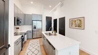 Located at 120 Kindley St in downtown Raleigh, NC, this thoughtfully designed one-bedroom, one-bathroom residence offers a well-appointed single-floor layout that maximizes both function and style. The open-concept living and kitchen area forms the heart of the home, anchored by soaring ceilings and recessed lighting that create a bright, airy atmosphere. The kitchen is a standout feature, equipped with gray shaker-style cabinetry, a white quartz waterfall island with an undermount sink, subway tile backsplash, and stainless steel appliances including a full-size refrigerator, range, microwave, and dishwasher. A sleek linear pendant light adds a modern touch overhead. The living room flows seamlessly toward a sliding glass door that opens to a private balcony overlooking lush greenery, with large windows that flood the space with natural light. Light wood flooring runs throughout, tying the spaces together cohesively. The bedroom is a serene retreat with tall windows, ample natural light, and generous closet space supported by a dedicated walk-in closet with wire shelving. The bathroom features a glass-enclosed, marble-tiled walk-in shower, clean white finishes, and light wood flooring, offering a spa-like feel. A hallway connects all spaces efficiently, completing this well-designed urban residence.