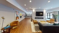 The Club Room at 1901 Elizabeth Ave in Rahway, NJ is a thoughtfully designed, single-floor community amenity space that blends modern aesthetics with a wide variety of social and recreational functions. Rich hardwood flooring flows throughout, unifying each distinct zone while recessed lighting and large floor-to-ceiling sliding glass doors flood the interior with natural light and provide views of the surrounding building exterior.

The lounge area serves as a central gathering point, featuring a sleek linear fireplace, a wall-mounted flat-screen television, and an eclectic mix of leather and upholstered seating arrangements. Vibrant framed artwork lines the walls, adding a curated, gallery-like quality to the space.

Adjacent to the lounge, a fully equipped kitchen showcases an expansive quartz countertop island, custom gray cabinetry with glass-front upper sections, a tile backsplash, stainless steel appliances including a professional-grade gas range and French door refrigerator, and pendant globe lighting overhead — making it well-suited for entertaining and catered events.

The game room area provides a dedicated space for recreation, complete with a shuffleboard table, ping-pong table, billiards table, and foosball table, all set against a backdrop of bold abstract artwork. Comfortable seating nooks are nestled throughout, offering quieter retreats within this expansive and versatile community gathering space.