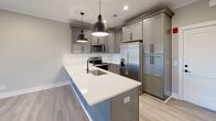 This single-story home in Lynchburg, Virginia offers a thoughtfully designed layout with modern finishes throughout. Light gray luxury vinyl plank flooring runs through the main living areas, creating a cohesive and contemporary aesthetic complemented by neutral warm-gray walls and crisp white trim and crown molding.

The kitchen is a standout feature, showcasing gray shaker-style cabinetry with matte black hardware, a white quartz peninsula with an undermount sink, and a full suite of stainless steel appliances including a refrigerator, range, and microwave. Industrial-style pendant lights hang above the peninsula, adding a modern touch. Ample cabinetry, including a tall pantry cabinet, provides generous storage.

The living areas are open and airy, each equipped with ceiling fans and recessed lighting. One room features elegant French doors with slatted blinds, flooding the space with natural light and providing outdoor access. The entryway area includes a large double-door closet and direct access to the exterior.

The bedrooms are carpeted in soft gray, offering a comfortable and quiet retreat. Each bedroom includes a ceiling fan and natural light from well-sized windows with blinds. The overall design is clean, move-in ready, and well-suited for comfortable everyday living.