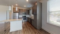 Located at 824 Finsbury St in Durham, NC, this single-story residence presents a clean, contemporary design with a neutral color palette and consistent attention to finish quality throughout. The kitchen serves as a central highlight, equipped with stainless steel appliances including a refrigerator, range, microwave, and dishwasher. Dark-toned cabinetry with ample tall storage panels complements the granite countertops and a peninsula that opens toward the dining and living areas. Pendant lighting accents the kitchen space, while recessed lighting adds functional illumination. Wood-look plank flooring extends through the main living areas and kitchen, providing a warm, cohesive aesthetic.

The living and dining areas are bright and open, benefiting from multiple windows fitted with horizontal blinds that allow natural light to filter throughout. Ceiling fans with integrated lighting are present in several rooms, contributing to both comfort and practicality. Bedrooms feature plush neutral carpeting and individual windows with outdoor views.

The bathrooms are well-appointed, with the primary bath offering a double-sink vanity topped with granite, a glass-enclosed walk-in shower, and wood-look flooring. A secondary bathroom provides additional convenience. Clean white walls and generous baseboards maintain a polished, move-in-ready appearance throughout the entire space.