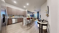 Located on LPGA Boulevard in Daytona Beach, Florida, this one-bedroom, one-bathroom unit offers a well-designed open-concept layout across a single floor. Light-toned wood-style flooring flows throughout, unifying the living, dining, and kitchen areas into a cohesive, airy space.

The kitchen is a standout feature, equipped with a full suite of stainless steel appliances—including a French door refrigerator, range, microwave, and dishwasher—complemented by taupe shaker-style cabinetry extending to the ceiling, white quartz countertops, a tile backsplash, and a peninsula with bar seating. The open living area is anchored by a striking accent wall featuring a nature-inspired mural, with a ceiling fan overhead and windows admitting natural light.

The bedroom is a comfortable, well-proportioned retreat with wood-style flooring, windows with window treatments, and access to a dedicated walk-in closet outfitted with wire shelving systems on multiple walls. The bathroom features large-format tile flooring, a taupe wood vanity with quartz countertop, and a glass-enclosed walk-in shower.