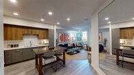 This contemporary single-floor residence at 1725 W Katella Ave in Orange, California, offers a thoughtfully designed open-concept layout that seamlessly connects the kitchen, dining, and living areas. The kitchen is a standout feature, outfitted with warm wood cabinetry, gray lower cabinets, stainless steel appliances including a refrigerator, gas range, microwave, and dishwasher, and a dark-topped island with bar seating — ideal for both cooking and casual dining. Light wood-style flooring runs throughout, lending a cohesive and modern feel to the entire space. The living room is bright and inviting, anchored by large windows that allow natural light to filter in and offer views of the outdoor surroundings. A clean hallway with recessed lighting connects the main living areas to the private quarters. The bedroom is generously proportioned, featuring a window with outdoor views, access to a walk-in closet, and clean white walls that create a calm and restful atmosphere. The bathroom presents a dual-sink vanity with gray cabinetry, white countertops, and framed mirrors, combining functionality with a polished aesthetic. Throughout the residence, recessed lighting, neutral tones, and modern fixtures contribute to a cohesive, contemporary ambiance well-suited to comfortable everyday living.