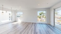 Located at 105-112 Avenida Mateo in the coastal community of San Clemente, California, this modern single-story home offers a thoughtfully designed layout with 3 bedrooms, 4 bathrooms, and an expansive floor plan that provides a true sense of openness and comfort. The interior is finished with light wood-tone flooring throughout, crisp white walls, and recessed lighting that enhances the bright, airy atmosphere across every room. The main living area is notably spacious, featuring large floor-to-ceiling sliding glass doors and multiple windows that frame views of the surrounding neighborhood's palm-lined streets, flooding the space with natural light. Elegant pendant lighting adds a refined touch overhead. The home includes two full kitchens, each showcasing contemporary design. The primary kitchen is a standout, equipped with a large center island with a gas cooktop, stainless steel appliances including a double oven and French door refrigerator, a sleek stainless range hood, and high-gloss white upper cabinetry paired with wood-toned lower cabinets. The bedrooms are well-proportioned and bright, with the primary suite offering walk-in closet space with built-in wire shelving systems. Large windows in the bedrooms capture neighborhood and palm tree views. With two closets, two hallways, and four full bathrooms, this home delivers practical functionality alongside its modern coastal aesthetic.