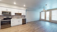 This single-floor residence presents a clean, modern aesthetic defined by consistent finishes and an open, functional layout. The kitchen serves as a central highlight, outfitted with crisp white shaker-style cabinetry accented by black hardware, a gray subway tile backsplash, and light-toned countertops. A full suite of stainless steel GE appliances—including a refrigerator, range, over-the-range microwave, and dishwasher—provides practical convenience. Recessed lighting illuminates the kitchen, which flows seamlessly into the living area via light-toned luxury vinyl plank flooring, creating a cohesive and open feel. The living space benefits from a ceiling fan and a large window fitted with blinds that allows natural light to fill the room.

The bedroom is generously sized, featuring plush carpet flooring, a ceiling fan, and a window for additional natural light. It connects to a walk-in closet outfitted with built-in shelving and dual hanging rods, offering substantial storage capacity. The bathroom maintains the unit's modern palette with a white vanity, light quartz-style countertop, black hardware, a large mirror with bright overhead lighting, and wood-look flooring. Additional closet space is visible near the kitchen, further enhancing the overall storage options throughout the unit.