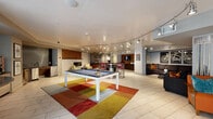 Located at 2131 Lawrence St in Denver's vibrant Five Points neighborhood, this single-floor community amenity space is designed for social gathering and relaxation. The open-plan layout is anchored by a central pool table set atop a bold, multicolored area rug, serving as the focal point of the room. Curved track lighting runs throughout the ceiling, providing dynamic, adjustable illumination across each zone of the space.

A curved bar with a dark stone countertop and red upholstered swivel stools offers a casual gathering spot, positioned near a flat-screen TV and a coffee station along the back wall. Adjacent to the bar, a cozy lounge area features a linear fireplace framed by a textured wood accent wall, complemented by cream lounge chairs arranged on a circular rug.

A large sectional sofa anchors a separate seating area, adorned with decorative framed artwork and accent pillows. Nearby, vibrant teal wingback chairs and a round pedestal table occupy a sunlit nook enclosed by floor-to-ceiling glass walls and doors, offering direct views of an outdoor pool area. Throughout the space, light tile flooring, eclectic artwork, and a rich palette of teal, orange, and red create a contemporary and energetic atmosphere.