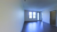 Located at 1020 N High St in Columbus, Ohio's dynamic Short North Arts District, this single-floor unit offers a clean, modern aesthetic designed for comfortable urban living. The main living area is bright and open, showcasing rich hardwood-style flooring that runs throughout the space, complementing the neutral, light-toned walls and creating a warm yet contemporary atmosphere. Natural light pours in through a set of double windows, illuminating the room and providing views to the outdoors. An adjacent door with a slatted blind offers additional access or ventilation, adding both functionality and flexibility to the layout. The space features smooth ceilings with recessed lighting, contributing to a polished, well-finished look. The clean lines and understated design palette make the space highly versatile, allowing for a range of interior arrangements. A connecting doorway leads further into the unit, suggesting additional rooms beyond the main living area. Situated in one of Columbus's most walkable and vibrant neighborhoods, this space benefits from proximity to local restaurants, galleries, and entertainment venues along the iconic High Street corridor.