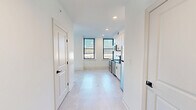 Located at 142 W York St in Norfolk, VA, this thoughtfully designed one-bedroom, two-bathroom unit offers a clean, modern aesthetic throughout. The open-concept layout seamlessly connects the dining room, kitchen, and living room, creating a bright and functional shared space bathed in natural light from large black-framed windows with city views. Light-toned tile flooring runs throughout, complementing the crisp white walls and contemporary finishes.

The kitchen is a standout feature, showcasing white shaker cabinetry with matte black hardware, dark granite countertops, a striking navy vertical tile backsplash, and a gold-accented faucet. Stainless steel appliances — including a refrigerator, dishwasher, electric range, and built-in microwave — complete the space.

The bedroom is a comfortable retreat with a ceiling fan and a dedicated window framing outdoor views. Two bathrooms provide added convenience: one full bath with a soaking tub/shower combo and matte black fixtures, and a second bathroom with a vanity and toilet. A louvered-door closet conceals a stacked in-unit washer and dryer. The entrance hallway provides a welcoming transition into this well-appointed, move-in-ready urban residence.