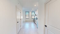 Located at 142 W York St in Norfolk, VA, this thoughtfully designed one-bedroom, two-bathroom unit offers a clean, modern aesthetic throughout. The open-concept layout seamlessly connects the dining room, kitchen, and living room, creating a bright and functional shared space bathed in natural light from large black-framed windows with city views. Light-toned tile flooring runs throughout, complementing the crisp white walls and contemporary finishes.

The kitchen is a standout feature, showcasing white shaker cabinetry with matte black hardware, dark granite countertops, a striking navy vertical tile backsplash, and a gold-accented faucet. Stainless steel appliances — including a refrigerator, dishwasher, electric range, and built-in microwave — complete the space.

The bedroom is a comfortable retreat with a ceiling fan and a dedicated window framing outdoor views. Two bathrooms provide added convenience: one full bath with a soaking tub/shower combo and matte black fixtures, and a second bathroom with a vanity and toilet. A louvered-door closet conceals a stacked in-unit washer and dryer. The entrance hallway provides a welcoming transition into this well-appointed, move-in-ready urban residence.