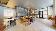 Located at 147 W Wood St in West Lafayette, Indiana, this single-floor space offers a generously sized, open-plan lobby and lounge that masterfully blends contemporary design with functional comfort. The terrazzo tile flooring spans the entire area, lending a polished, cohesive aesthetic throughout.

At the heart of the space is a welcoming lobby seating area anchored by a bold, multicolored geometric rug and mustard-toned modular sofas, accented by a curved frosted-glass partition that adds architectural depth. Pendant and linear lighting fixtures illuminate the area with a warm, inviting glow.

The dining and lounge zone is a standout feature, highlighted by a dramatic chalkboard accent wall covered in mathematical equations and diagrams — a nod to the academic character of the surrounding community. Warm amber booth seating lines this wall, complemented by wood paneling, brass ceiling details, and pendant bulbs that create an intimate yet energetic atmosphere.

Lush indoor plants and raised planter beds are integrated throughout, adding vibrancy and a biophilic quality to the space. Large floor-to-ceiling windows and glass-paneled entry doors flood the interior with natural light and provide open views of the surrounding streetscape. A corridor with frosted feature walls connects distinct zones seamlessly, while private seating alcoves with statement pendant lamps offer quieter retreats within the larger open floor plan.