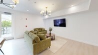 Located at 199 Gardner St in Boston, MA, this single-floor space offers a well-organized layout comprising a living room, dining room, bedroom, and office. The interior features a clean, modern aesthetic defined by light hardwood flooring, crisp white walls, and recessed lighting throughout.

The living room is a bright, welcoming area anchored by a stylish multi-arm chandelier, plush green sofas, and a wall-mounted flat-screen display — ideal for both relaxation and casual gatherings. Adjacent to it, the dining room is appointed with a warm wood table and neutral upholstered seating, set against subtly patterned wallpaper that adds texture without overwhelming the space.

A dedicated office, enclosed by elegant black-framed glass partition doors, provides a private and focused work environment with views to the hallway. The bedroom is generously proportioned, offering a comfortable and private retreat. The hallway connects all areas efficiently, with direct access to an exterior door that brings in abundant natural light and views of the surrounding neighborhood.

Throughout the space, large windows with dark-framed casings invite natural light and outdoor views, creating an airy, contemporary ambiance. The cohesive use of neutral tones, modern fixtures, and thoughtful design details make this a highly functional and visually refined space.