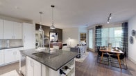 This single-floor residence showcases a thoughtfully designed open-concept layout that seamlessly connects the kitchen, living, and dining areas. The kitchen is a standout feature, equipped with white shaker-style cabinetry extending to the ceiling, dark granite countertops, a light blue subway tile backsplash, stainless steel appliances, and a peninsula with an undermount sink and pendant lighting overhead. A dedicated wine rack is integrated into the peninsula's base, adding a refined touch.

The living area is anchored by wood-style flooring, an accent wall, and access to a private patio through glass doors dressed with patterned drape panels. Two bedrooms offer comfortable retreats; the primary bedroom features a ceiling fan, natural light from multiple windows, and a neutral accent wall. A second bedroom mirrors this comfortable aesthetic.

Two full bathrooms serve the residence — one featuring a frameless glass walk-in shower with dark vanity and granite countertop, and the other offering a soaking tub with dark cabinetry and matching granite surfaces. A dedicated laundry room houses a full-size side-by-side washer and dryer with built-in shelving above for additional storage.