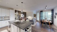 This single-floor residence showcases a thoughtfully designed open-concept layout that seamlessly connects the kitchen, living, and dining areas. The kitchen is a standout feature, equipped with white shaker-style cabinetry extending to the ceiling, dark granite countertops, a light blue subway tile backsplash, stainless steel appliances, and a peninsula with an undermount sink and pendant lighting overhead. A dedicated wine rack is integrated into the peninsula's base, adding a refined touch.

The living area is anchored by wood-style flooring, an accent wall, and access to a private patio through glass doors dressed with patterned drape panels. Two bedrooms offer comfortable retreats; the primary bedroom features a ceiling fan, natural light from multiple windows, and a neutral accent wall. A second bedroom mirrors this comfortable aesthetic.

Two full bathrooms serve the residence — one featuring a frameless glass walk-in shower with dark vanity and granite countertop, and the other offering a soaking tub with dark cabinetry and matching granite surfaces. A dedicated laundry room houses a full-size side-by-side washer and dryer with built-in shelving above for additional storage.