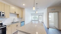 This well-designed one-bedroom, two-bathroom unit offers an efficient and modern single-floor layout. The open-concept kitchen and living area forms the heart of the unit, where light wood-tone cabinetry, a tile backsplash, and stainless steel appliances — including a range, microwave, and dishwasher — provide a clean, contemporary aesthetic. A large granite-style island with pendant lighting overhead anchors the kitchen, creating a natural transition into the living area. The living space features light hardwood-style flooring, a ceiling fan, and a wall of windows alongside a glass door that opens to a private balcony, allowing abundant natural light and outdoor views.

The bedroom is a comfortable size, finished with plush carpeting, a ceiling fan, and a window that brings in additional natural light. Two full bathrooms serve the unit, one featuring a soaking tub with a tiled surround. A dedicated in-unit laundry area houses a full-size washer with overhead wire shelving. Throughout the unit, a neutral white and warm beige palette, consistent flooring materials, and clean architectural lines contribute to a bright, cohesive, and move-in-ready living environment.