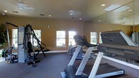 This fitness center offers a practical and well-appointed space designed to support a variety of workout routines. The room is finished with warm-toned walls and carpeted flooring, creating a comfortable environment for exercise. Recessed ceiling lights, complemented by a central ceiling fixture, provide consistent illumination throughout the space, while multiple windows along the walls invite natural light and outdoor views, enhancing the overall ambiance. A large wall-mounted mirror spans one side of the room, visually expanding the space and allowing users to monitor their form during workouts. The equipment selection is well-rounded, featuring treadmills, a stationary cycle, and a multi-function strength training machine, catering to both cardio and resistance training needs. The layout is thoughtfully arranged to allow comfortable movement between stations. The single-floor layout keeps everything accessible and easy to navigate. Whether used for a focused cardio session or a full-body strength workout, this fitness center provides a functional and inviting setting equipped to meet a range of fitness goals.