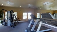 This fitness center offers a practical and well-appointed space designed to support a variety of workout routines. The room is finished with warm-toned walls and carpeted flooring, creating a comfortable environment for exercise. Recessed ceiling lights, complemented by a central ceiling fixture, provide consistent illumination throughout the space, while multiple windows along the walls invite natural light and outdoor views, enhancing the overall ambiance. A large wall-mounted mirror spans one side of the room, visually expanding the space and allowing users to monitor their form during workouts. The equipment selection is well-rounded, featuring treadmills, a stationary cycle, and a multi-function strength training machine, catering to both cardio and resistance training needs. The layout is thoughtfully arranged to allow comfortable movement between stations. The single-floor layout keeps everything accessible and easy to navigate. Whether used for a focused cardio session or a full-body strength workout, this fitness center provides a functional and inviting setting equipped to meet a range of fitness goals.