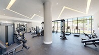 Located at 5961 SW 68th St in South Miami, FL, this professionally designed fitness center offers a generous, open-plan workout space across a single floor. The facility is characterized by its modern architectural design, featuring soaring ceilings with striking geometric recessed LED lighting that creates a bright, energizing atmosphere throughout.

Floor-to-ceiling glass windows line multiple walls, flooding the interior with abundant natural light and providing open views of the surrounding greenery and streetscape. The durable rubber-speckle flooring provides a practical and resilient surface suited to a full range of fitness activities.

A prominent central column adds a structural architectural element that naturally divides the space into distinct workout zones without enclosing them. The strength training area is well-equipped with a multi-station cable machine, selectorized weight machines, a free weight rack, and adjustable benches. The cardio zone features a row of Matrix-brand ellipticals, treadmills, and stationary bikes positioned to take full advantage of the natural light from the large windows.

A vibrant athletic-themed mural in bold teal and white anchors one wall, adding visual energy to the space. A dedicated area near the entrance accommodates stability balls and Smart Fitness equipment. Double glass doors provide easy access to an adjacent outdoor area. The overall ambiance is clean, contemporary, and motivating — purpose-built for an active lifestyle.