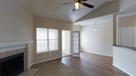 This single-story space showcases an open, airy layout highlighted by vaulted ceilings that enhance the sense of volume and spaciousness. The main living area features durable hardwood-style flooring in a warm, dark tone, while a carpeted section near the entry provides a subtle transition between zones. A ceiling fan with a light fixture is centrally positioned in the main area, offering both comfort and illumination, while a pendant light fixture serves the adjoining room.

A striking French door with a grid-pane design connects the two living areas, allowing natural light to flow freely between spaces while maintaining a sense of definition. Horizontal blinds on the double window filter natural light effectively, contributing to a bright yet controlled atmosphere. The neutral, beige-toned walls complement the overall palette and provide a versatile backdrop.

The textured popcorn ceiling adds a classic residential character, and white baseboards frame the flooring throughout. The layout appears well-suited for both relaxed everyday living and functional use, with adequate outlets and open wall space offering flexibility in furnishing and arrangement.