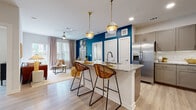 This single-floor residence showcases a thoughtfully designed open-concept layout where the kitchen flows seamlessly into the dining and living areas. The kitchen is a standout feature, equipped with stainless steel appliances, taupe shaker-style cabinetry, a white subway tile backsplash, and a generously sized granite-topped island with an undermount sink. Pendant lights with gold accents hang above the island, adding a stylish touch. A bold teal accent wall anchors the kitchen-dining transition, creating a vibrant focal point.

The living room is bright and welcoming, with light-toned walls, light wood-style flooring, and a sliding glass door that invites natural light and outdoor views. A ceiling fan enhances comfort throughout the shared living space.

Both bedrooms are comfortably sized with large windows dressed in sheer curtains that allow ample natural light. Light wood-style flooring carries throughout both rooms, contributing to a cohesive aesthetic.

The two bathrooms feature granite-topped vanities with taupe cabinetry. The primary bathroom includes a walk-in closet, while the secondary bathroom offers a tub-shower combination. Clean white walls and light flooring give both bathrooms a fresh, polished look.