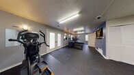 Located at 4016 W Michigan Ave in Kalamazoo, Michigan, this single-floor fitness center is a well-equipped workout facility designed to support a full range of exercise activities. The main workout area is generously sized, featuring durable rubber flooring throughout that provides comfort and safety during training sessions. The space is brightly lit with overhead fluorescent lighting and accented by wall-mounted sconces, ensuring excellent visibility across the room.

The cardio section houses multiple treadmills, stair climbers, and elliptical machines, offering a variety of options for cardiovascular training. A dedicated free weights area includes a full rack of dumbbells in graduated sizes, a workout bench, and a stability ball, all positioned in front of a large wall-to-wall mirror that enhances the sense of space and allows users to monitor their form. Natural light filters in through several windows, adding to the open, energizing atmosphere.

The facility features a motivational "No Pain, No Gain" wall decal, reinforcing the fitness-focused environment. A security camera is mounted overhead for safety. Access is provided through both a set of frosted glass French doors and a standard entry door. A conveniently located restroom with light wood-tone flooring, vanity with sink, and toilet rounds out the amenities, making this a fully functional and self-contained fitness space.