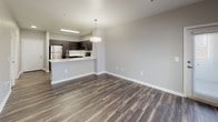 Located at 10001 E Dry Creek Rd in Englewood, Colorado, this modern single-floor unit offers a thoughtfully designed layout that balances style and functionality. The open-concept living and kitchen area serves as the heart of the space, where rich, dark wood-style flooring flows seamlessly underfoot. The kitchen is outfitted with sleek dark cabinetry extending to the upper walls, a full suite of stainless steel appliances including a refrigerator, range, and microwave, and a light-toned countertop that wraps around to a peninsula — ideal for casual dining or food prep. A pendant light fixture adds a modern focal point above the kitchen area.

The bedrooms offer a comfortable retreat, with plush carpeting, neutral gray walls, and natural light filtering through wide windows fitted with horizontal blinds. A ceiling fan in one bedroom adds both comfort and a finishing touch. An in-unit laundry area provides added convenience.

The bathroom features the same wood-style flooring found throughout the main living spaces, paired with a dark vanity cabinet, a white countertop with an undermount sink, brushed nickel fixtures, and a full-size soaking tub with a shower. Clean white walls and a large vanity mirror complete the polished look. Throughout the unit, neutral tones and contemporary finishes create a cohesive, modern aesthetic.