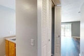 This efficiently designed single-floor unit offers a well-organized layout that makes smart use of its intimate footprint. The combined kitchen and living area forms the heart of the space, where rich hardwood-style plank flooring flows throughout and provides a warm, cohesive aesthetic. The living area is bright and open, benefiting from generous natural light that pours in through large sliding glass doors. These doors open to an outdoor view and are complemented by vertical blinds for privacy. A wall-mounted mini-split air conditioning unit and a baseboard heating system provide year-round climate control.

The kitchen is positioned at one end of the main living space, separated by a half-wall peninsula counter that doubles as a breakfast bar. Warm honey-toned wood cabinetry lines the upper and lower walls, offering ample storage, and is paired with white appliances including a refrigerator and a range. A dedicated overhead range hood and recessed lighting keep the kitchen functional and well-lit.

The bathroom features a wood-toned vanity with a white countertop sink, a well-lit mirror with a multi-bulb vanity light fixture, and hardwood-style flooring that ties in with the rest of the unit. A louvered bi-fold closet door in the hallway provides convenient storage access, rounding out this practical and well-appointed space.