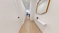 This thoughtfully designed single-floor residence showcases a clean, contemporary aesthetic carried consistently throughout every room. Light oak hardwood flooring runs seamlessly from the entry hallway through the main living spaces, complemented by crisp white walls and recessed lighting that create a bright, airy atmosphere.

The open-concept kitchen is a standout feature, equipped with white shaker-style cabinetry extending to the ceiling for ample storage, a large central island with a grey quartz countertop and bar seating for two, and a full suite of stainless steel Bosch appliances including a gas range, built-in microwave, refrigerator, and dishwasher. A sleek matte black pendant light anchors the island, while a marble-look tile backsplash adds an elegant touch.

The kitchen flows naturally into the dining area and living room, which is bathed in natural light from oversized windows fitted with roller shades. The bedroom continues the same refined palette, featuring large windows that bring in abundant light.

The bathroom is finished with floor-to-ceiling linear tile in soft neutral tones, paired with a soaker tub and a matte black handheld shower fixture and hardware, delivering a spa-like quality. A clean, well-lit hallway connects all areas of the unit efficiently.
