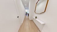 This thoughtfully designed single-floor residence showcases a clean, contemporary aesthetic carried consistently throughout every room. Light oak hardwood flooring runs seamlessly from the entry hallway through the main living spaces, complemented by crisp white walls and recessed lighting that create a bright, airy atmosphere.

The open-concept kitchen is a standout feature, equipped with white shaker-style cabinetry extending to the ceiling for ample storage, a large central island with a grey quartz countertop and bar seating for two, and a full suite of stainless steel Bosch appliances including a gas range, built-in microwave, refrigerator, and dishwasher. A sleek matte black pendant light anchors the island, while a marble-look tile backsplash adds an elegant touch.

The kitchen flows naturally into the dining area and living room, which is bathed in natural light from oversized windows fitted with roller shades. The bedroom continues the same refined palette, featuring large windows that bring in abundant light.

The bathroom is finished with floor-to-ceiling linear tile in soft neutral tones, paired with a soaker tub and a matte black handheld shower fixture and hardware, delivering a spa-like quality. A clean, well-lit hallway connects all areas of the unit efficiently.