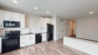 Located at 307 Debaliviere Ave, Unit N412, in St. Louis, Missouri, this single-floor unit offers a clean, contemporary design with consistent finishes throughout. The open-concept layout connects the kitchen and living areas seamlessly, creating a functional and visually cohesive space.

The kitchen is outfitted with white shaker-style cabinetry, dark countertops, and a full suite of black appliances, including a refrigerator, electric range, built-in microwave, and dishwasher. A stainless steel sink with a modern faucet anchors the workspace, while recessed lighting overhead provides ample illumination. Light wood-look luxury vinyl plank flooring extends throughout the unit, adding warmth and continuity.

The living area features large windows fitted with horizontal blinds, allowing natural light to fill the space. A built-in low-profile ledge runs along one wall, offering practical surface space. The room provides a versatile, open footprint well-suited for varied furniture arrangements.

The bathroom includes a white vanity with black hardware, a wall-mounted toilet, and a shower-tub combination enclosed by a sliding glass door, all finished with matching wood-look flooring. Interior doors feature a clean panel design with matte black lever hardware, reinforcing the unit's modern aesthetic throughout.
