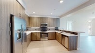 This contemporary single-floor residence offers a thoughtfully designed layout with clean lines and modern finishes throughout. The kitchen serves as a functional centerpiece, featuring wood-grain flat-front cabinetry extending to the ceiling, stainless steel appliances including a gas range, built-in microwave, dishwasher, and refrigerator, complemented by white quartz countertops and a metallic tile backsplash. Light hardwood-style flooring carries through the kitchen and into the open living area, which offers a bright, open canvas with recessed lighting and a seamless connection to the kitchen via a peninsula counter. The bedrooms are finished with plush carpet and feature large windows that invite generous natural light and views of the surrounding neighborhood and greenery. One bedroom benefits from a corner window configuration, enhancing the sense of openness. The primary bathroom is well-equipped with a wide dual-sink vanity, wood-toned cabinetry, a large mirror, and modern lighting fixtures, with a tiled shower area visible beyond. A secondary bathroom provides a single-sink vanity, a tub-shower combination with built-in shelving, and light hardwood-style flooring. Throughout the space, a neutral color palette, consistent material selections, and clean architectural detailing create a cohesive, contemporary ambiance.