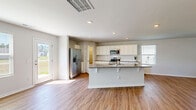 Located in a well-kept neighborhood in Bolivia, NC, this two-story home offers four bedrooms, three bathrooms, and a thoughtfully designed layout spread across two floors. The main level opens into a bright, open-concept kitchen and living area featuring durable hardwood-style flooring throughout. The kitchen is appointed with white shaker cabinetry, granite countertops, a large center island with seating, stainless steel appliances including a refrigerator with ice maker, microwave, and range, plus a tile backsplash. Natural light flows in through multiple windows, enhancing the airy feel of the main living space. A conveniently located half bath with a pedestal sink serves the first floor. An attached garage and dedicated laundry room with a full-size washer and dryer complete the lower level. Upstairs, the generously sized primary bedroom features two windows, a ceiling fan, hardwood-style flooring, and a walk-in closet with wire shelving. Three additional bedrooms offer plush carpeting and ample closet space. The home sits on a well-maintained lot with a concrete driveway and lawn, overlooking a quiet, established residential street lined with mature trees and green space.
