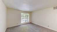 Located at 5125 47th Ave in Sacramento, CA, this single-story unit offers three bedrooms and two bathrooms across a practical, efficiently arranged floor plan. The combined kitchen and living room serves as the heart of the home, with the kitchen featuring white cabinetry, light stone-style countertops, a dishwasher, and a full-size refrigerator, all set on easy-care hard flooring. The adjacent living area is carpeted and benefits from a large window that invites natural light and outdoor views. Each of the three bedrooms is carpeted and includes its own window overlooking greenery outside, providing a calm and bright atmosphere. The spacious primary bedroom connects to a dedicated closet complete with a full-width hanging rod and soft carpet underfoot. The two bathrooms are clean and functional: one features a wide vanity with a stone-topped countertop, a large mirror, and hard flooring, while the other includes a full tub-shower combination with chrome fixtures. A hallway connects the rooms efficiently throughout the unit. Dark wood-toned interior doors with brass hardware add a classic contrast to the neutral white walls and textured ceilings found throughout the home.