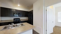 This single-floor residence offers a well-organized and functional layout designed for comfortable everyday living. The kitchen serves as a central highlight of the space, showcasing rich, dark espresso-toned cabinetry that contrasts elegantly with the light-toned countertops. A suite of black appliances — including a refrigerator, electric range, built-in microwave, and dishwasher — lends a cohesive, modern look to the culinary space. A peninsula-style counter extension provides additional workspace and doubles as a casual dining or serving area, complete with an integrated stainless steel sink. The cabinetry extends to the ceiling, maximizing storage capacity and contributing to the kitchen's clean, streamlined appearance. Hard flooring runs underfoot, adding durability and a contemporary touch to the space. The walls are finished in a neutral, crisp white palette that reflects light and creates an open, airy ambiance. Recessed lighting provides focused illumination throughout. The layout flows efficiently, with clear sightlines between functional zones, making the space practical and easy to navigate. Overall, the residence presents a tidy, move-in-ready environment with a modern design sensibility.