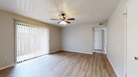 This single-floor unit offers a practical and well-organized layout, encompassing one bedroom, two bathrooms, a living room, dining room, kitchen, and hallway. Throughout the unit, light-toned wood-style flooring creates a cohesive, clean aesthetic that extends across all main living areas.

The living room serves as the central gathering space, featuring a ceiling fan with integrated lighting, a textured popcorn ceiling, and a full-length sliding glass door dressed with vertical blinds that allow ample natural light to filter in. The dining area adjoins the living space, providing a seamless open flow ideal for everyday living.

The kitchen is equipped with white cabinetry accented by brass hardware, a double stainless steel sink, and light wood-toned countertops. Upper and lower cabinet configurations offer functional storage throughout.

The spacious primary bedroom includes a ceiling fan, a window with blinds for natural light, and generous floor space. One of the bathrooms features a built-in vanity with a rich, marble-patterned countertop and a wall-mounted mirror, adding a distinctive detail to the space.

A connecting hallway links the rooms efficiently, contributing to the unit's compact yet organized flow.