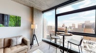Located in Chicago's 60605 neighborhood, this single-floor unit showcases a striking blend of industrial and contemporary design. The exposed concrete ceiling serves as a defining architectural element throughout the space, complementing the light wood-toned flooring that runs seamlessly from room to room.

The living area is anchored by floor-to-ceiling windows that frame sweeping elevated views of the Chicago skyline, flooding the space with abundant natural light. A bistro-style dining nook positioned directly at the window wall takes full advantage of the cityscape, making it an ideal spot for dining with a view.

The kitchen is efficiently designed with white cabinetry extending to the ceiling for generous storage, light quartz countertops, a stainless steel sink, and a full suite of stainless steel appliances including a gas range, over-the-range microwave, dishwasher, and refrigerator. Dark hardwood flooring in the kitchen adds a warm contrast to the clean cabinetry.

The bedroom features the same exposed concrete ceiling, crisp white walls, and dark hardwood flooring, offering a calm and modern retreat. The bathroom is cleanly appointed with a wood-toned vanity, mirror, and wood-look tile flooring, maintaining the cohesive modern aesthetic found throughout the unit.