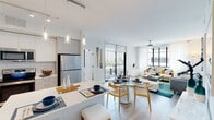 Located on the sixth floor at Kings Point Drive in Sunny Isles Beach, Florida, this 2-bedroom, 2.5-bathroom residence offers a thoughtfully designed open-concept layout with modern finishes throughout. Light wood flooring flows seamlessly from the entry through the main living areas, enhancing the bright and airy atmosphere.

The kitchen is a standout feature, boasting white flat-panel cabinetry, a white subway tile backsplash, stainless steel appliances, and a generous island with a quartz countertop that provides additional seating. Elegant pendant lighting illuminates the space, which opens directly into the dining and living areas. Large floor-to-ceiling windows and a sliding glass door to the balcony invite abundant natural light and outdoor views into the living room, which is further complemented by a ceiling fan.

Both bedrooms are well-proportioned, offering large windows with sheer drapery, light-toned flooring, and walk-in closet access. The primary bathroom features a sleek double-sink vanity with white cabinetry and a glass-enclosed walk-in shower with textured tile surround. A second full bathroom provides a dual-sink vanity with dual framed mirrors. A half bath adds everyday convenience. The building's sixth-floor corridor features a clean, contemporary design with bold navy blue walls and large-format tile flooring.