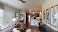 The B3 is a thoughtfully designed two-bedroom, two-bathroom floor plan that combines modern finishes with a functional open layout. Rich, dark hardwood-style flooring flows throughout the main living areas, anchoring the space with warmth and continuity. The open-concept kitchen is a standout feature, showcasing dark espresso cabinetry that extends to the ceiling, granite countertops, a full suite of stainless steel appliances, a tile backsplash, and a breakfast bar with pendant lighting overhead. The kitchen opens seamlessly into the living and dining areas, making it ideal for entertaining. The living room features a ceiling fan and generous natural light through large windows. Both bedrooms are well-proportioned, each with ceiling fans and ample natural light from multiple windows. The primary bathroom includes a walk-in glass-enclosed shower, while the secondary bathroom offers a shower-tub combination. Both bathrooms continue the granite and dark cabinetry design aesthetic seen throughout the home. A dedicated in-unit laundry area houses a full-size washer and dryer. The overall color palette of soft grays and warm neutrals creates a cohesive, contemporary ambiance throughout this single-story residence.