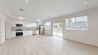 Located at 1301 E 27th St in Los Angeles, this contemporary three-story home offers five bedrooms and four bathrooms spread across three well-proportioned floors. Light wood-style flooring runs consistently throughout the interior, lending a clean, cohesive aesthetic to each level.

The ground floor houses the main living area and kitchen, which features white shaker cabinetry, a subway tile backsplash, stainless steel appliances including a gas range, dishwasher, and refrigerator, and recessed lighting overhead. A stacked washer and dryer unit is conveniently located on this level as well. The living area opens outward through a sliding glass door, providing direct access to outdoor space and views of the surroundings.

Upper floors contain the bedrooms, including a generously sized primary bedroom with a dedicated closet and access to a private balcony with sliding glass doors and ample natural light. Additional bedrooms are bright and well-proportioned, each with access to the stairwell featuring dark metal railings. Bathrooms are finished with marble-style tile, including a dramatic dark-veined marble surround in one shower enclosure, alongside white vanities with tile accents in others. Three closets provide practical storage throughout the home.